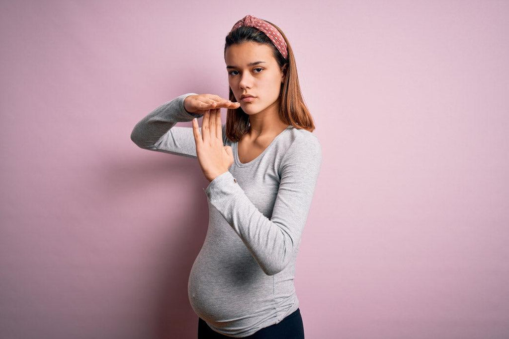 alt="When talking about disability words matter: a pregnant woman is standing against an isolated pink background doing a time out gesture with their hands. 