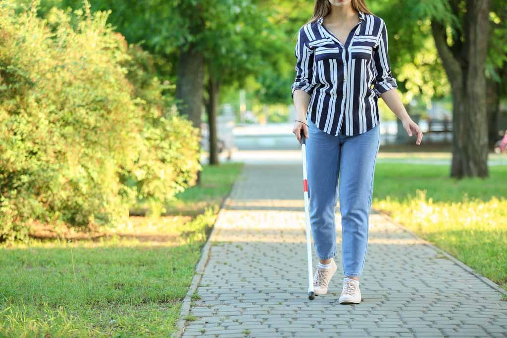 Color photo of a blind woman walking on footpath in an urban park
