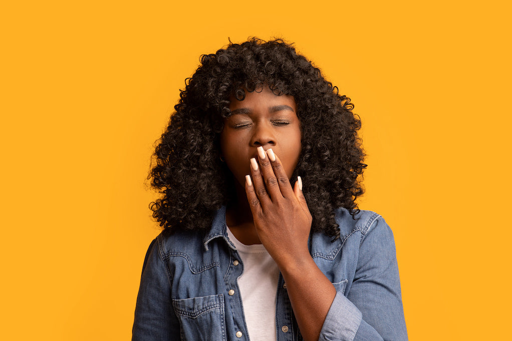 Dating someone with narcolepsy: a photo of a woman yawning against a yellow background, covering mouth with her hand.