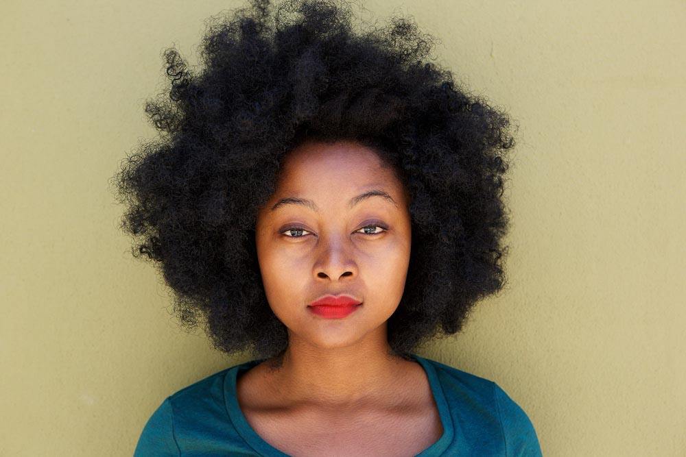 Close up serious young woman standing by wall with afro. Image for an article: Why is postpartum depression in black moms ignored in the U.S.