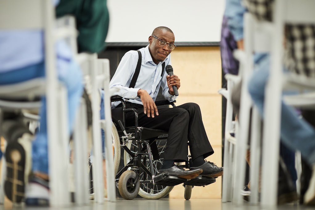 What is an ableist slur? A disabled Black scientist in glasses sitting in wheelchair and speaking into microphone while addressing a conference.