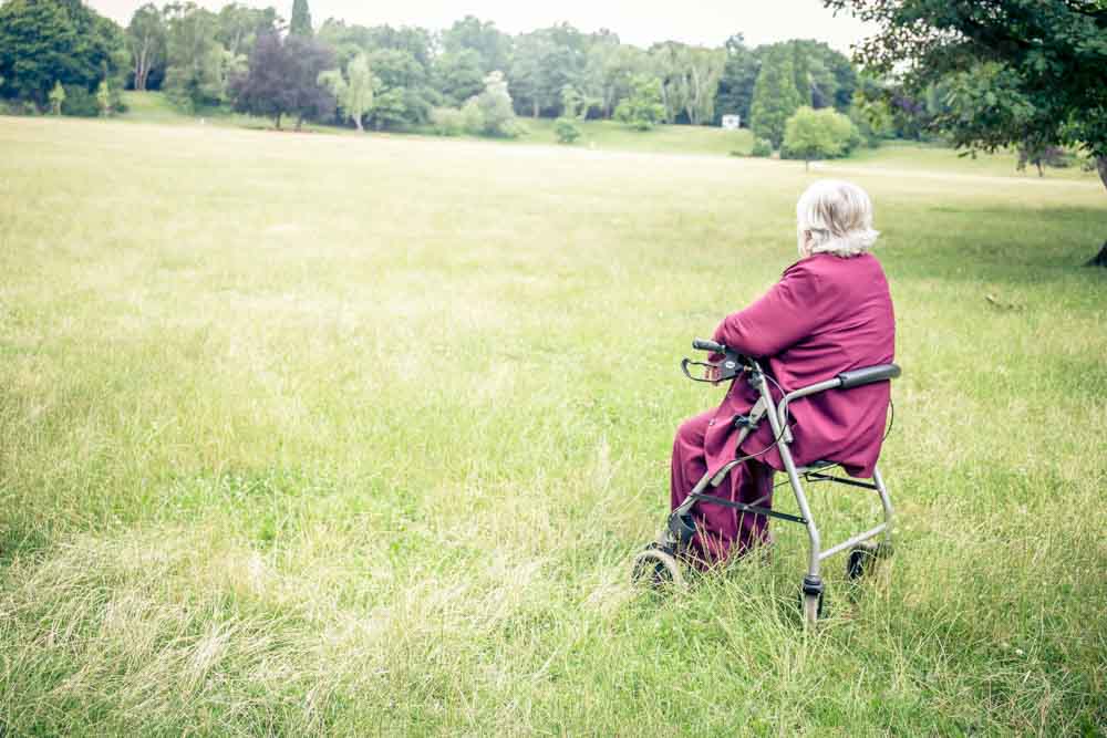 A woman is using a mobility aid in park. She is sitting down on her  Image result for walking frame chair combined A rollator is often called a "rolling walker with a seat". 