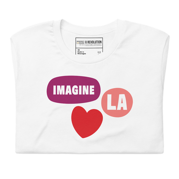 A close of a folded white Imagine LA shirt featuring the LA Imagine logo of three separate bubbles in the middle of the shirt. One bubble has the word Imagine, the second one has the acronym LA, and the third red bubble is in the shape of a heart.