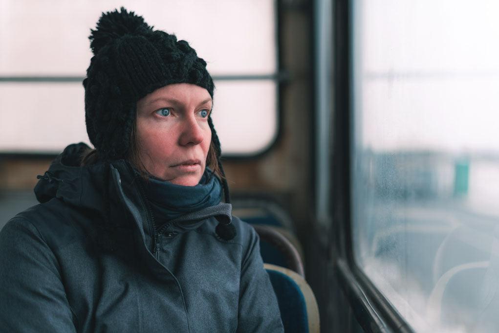 Public transport and mental disorders: a sad person on a bus is looking through window at the street on cold winter day.