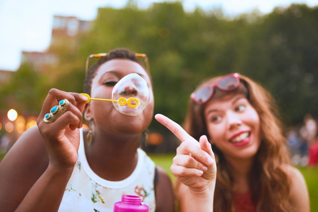 Meeting old friends when newly sober, a group of two diverse friends blow soap bubbles at a summer music festival.