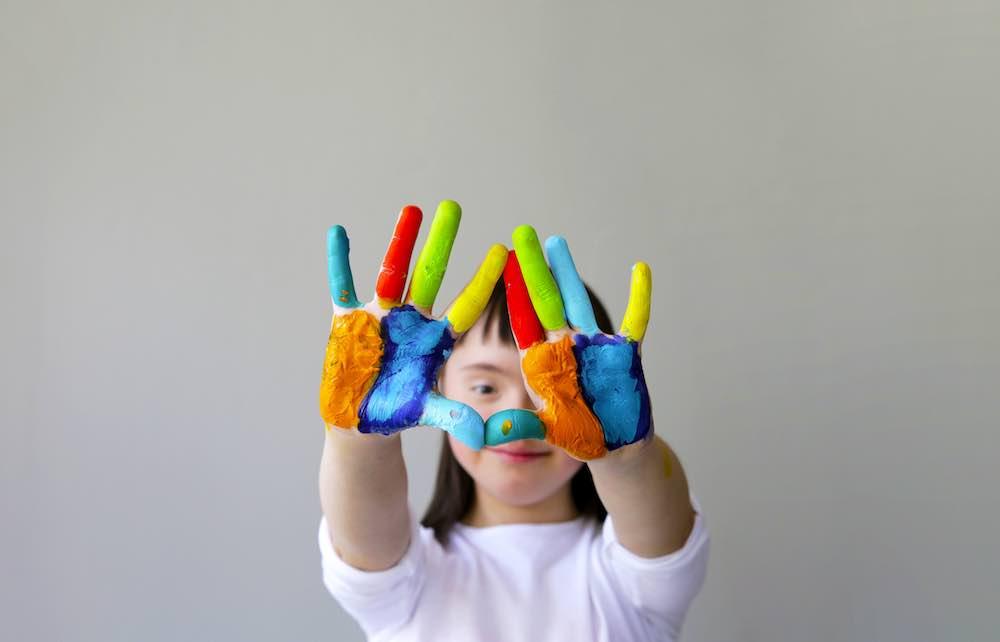 Photo for article about disability and infanticide. Photo of infant holding their colorful painted hands up as if to say stop.