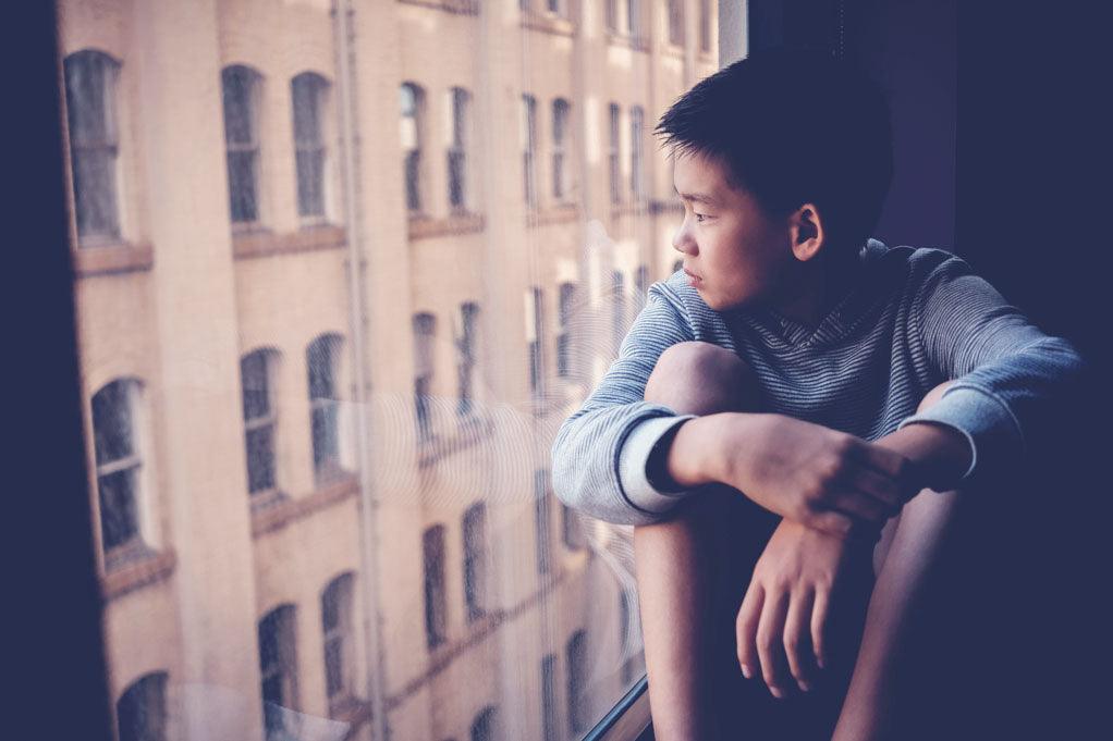 How to talk to my son. Sad Asian preteen boy feeling lonely, looking out of window from his room, social distancing, isolation, mental health concept.