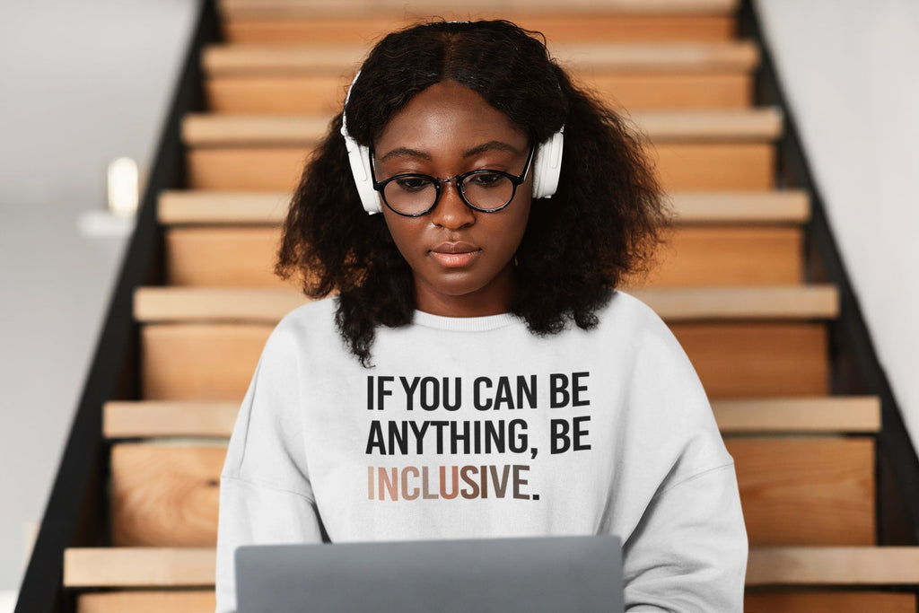 Autistic person or person with autism: a person wearing a "be inclusive" sweatshirt is sitting on some wooden steps while working on a laptop.