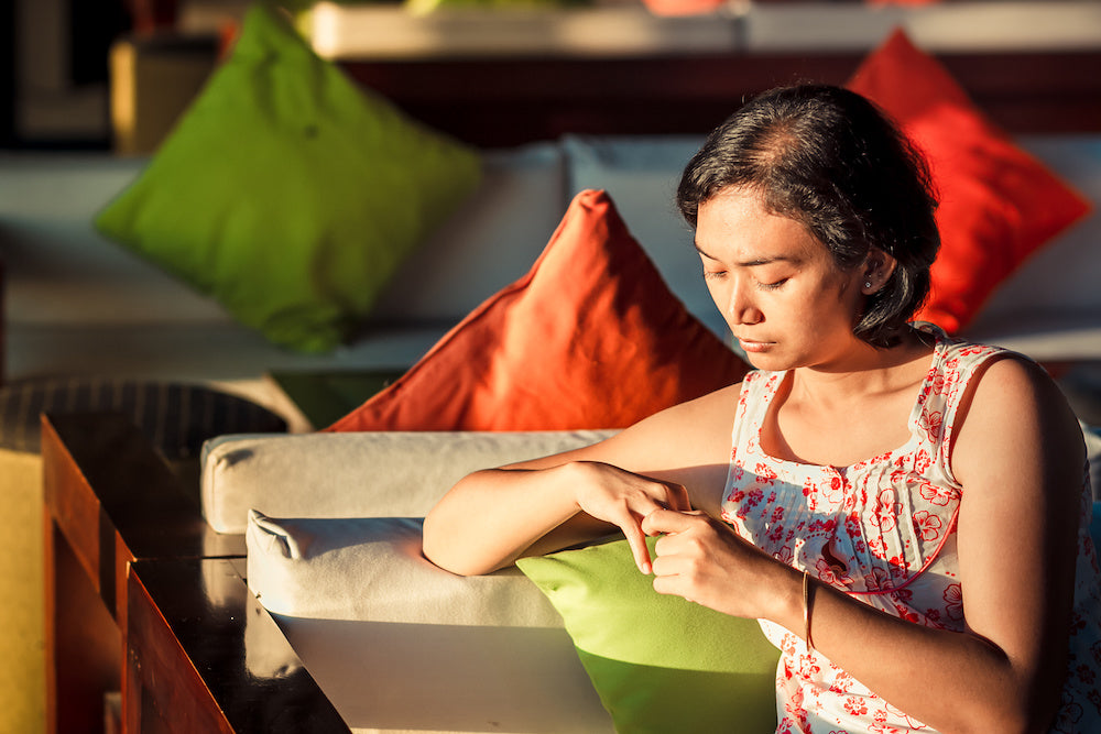 An Asian woman is sitting outside in the sun in deep thought thinking about balancing Eastern and Western cultural values for mental health.