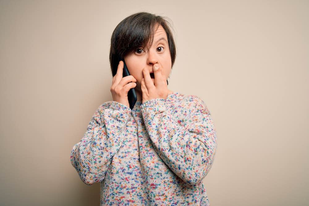 Photo for article on how to help someone with a disability. Photo of person with Down syndrome talking on a mobile phone with a slightly frustrated expression.