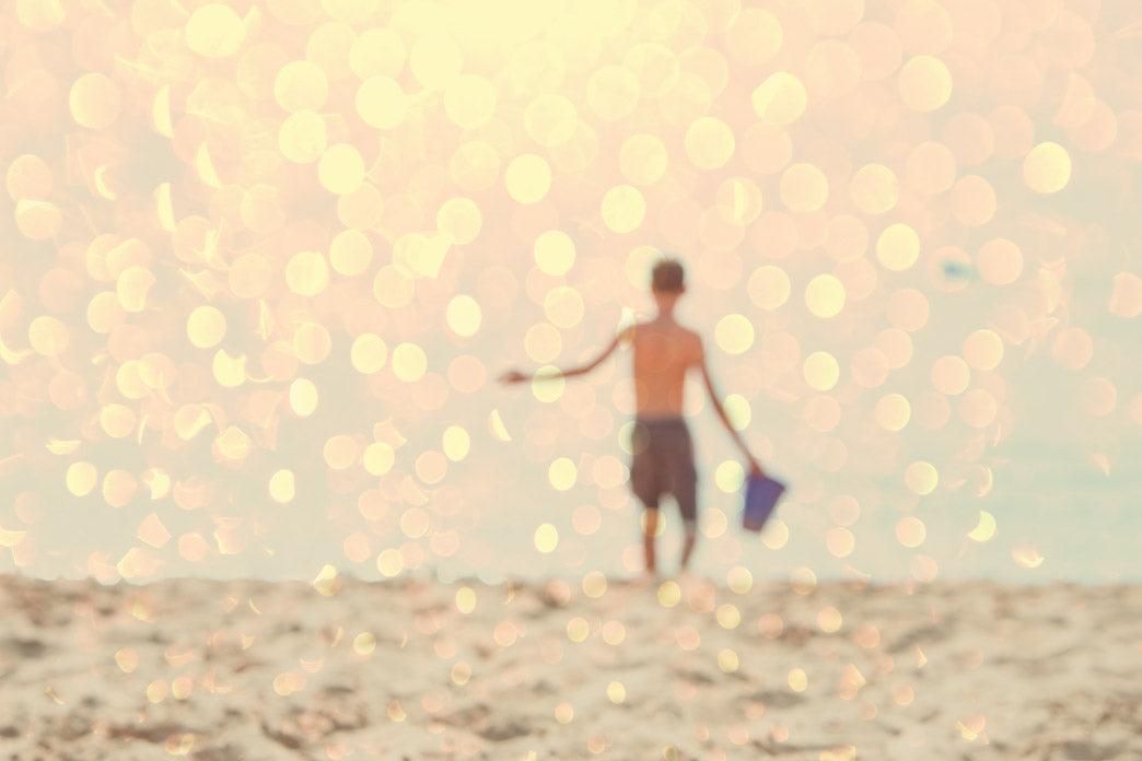A child stands on a beach in a softly focused, sunlit photograph.