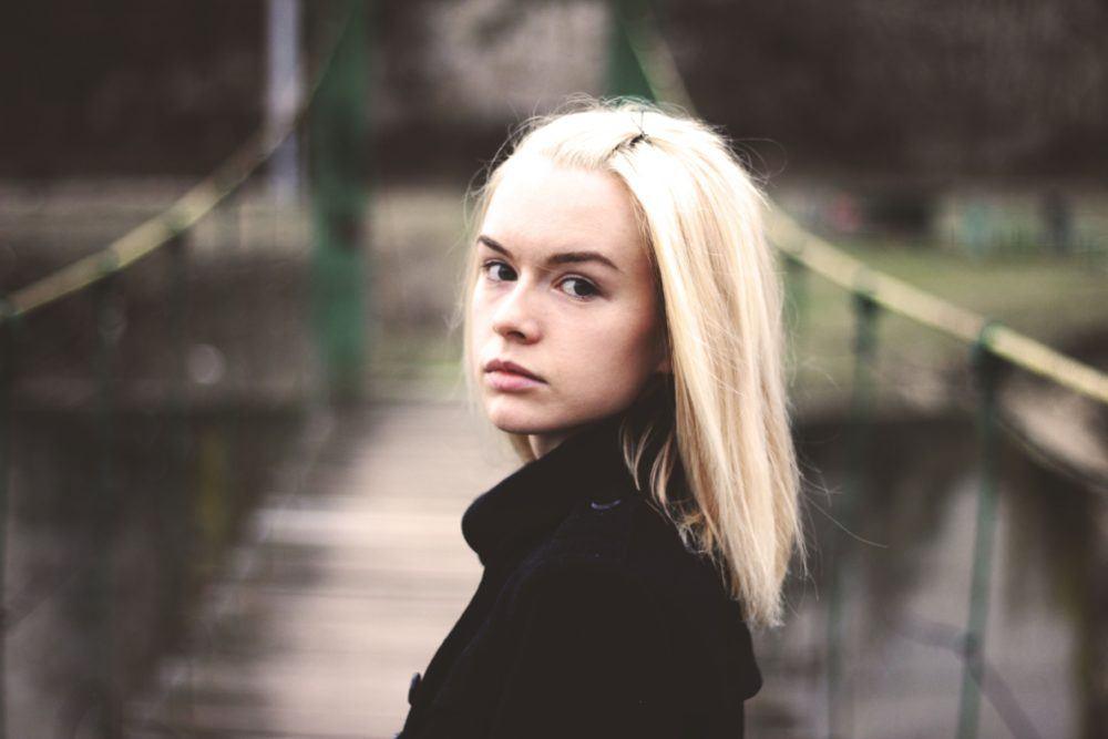 A teenager, with long flowing blonde hair, stands on a pedestrian suspension bridge. Image for an article: How common are eating disorders in Australia?