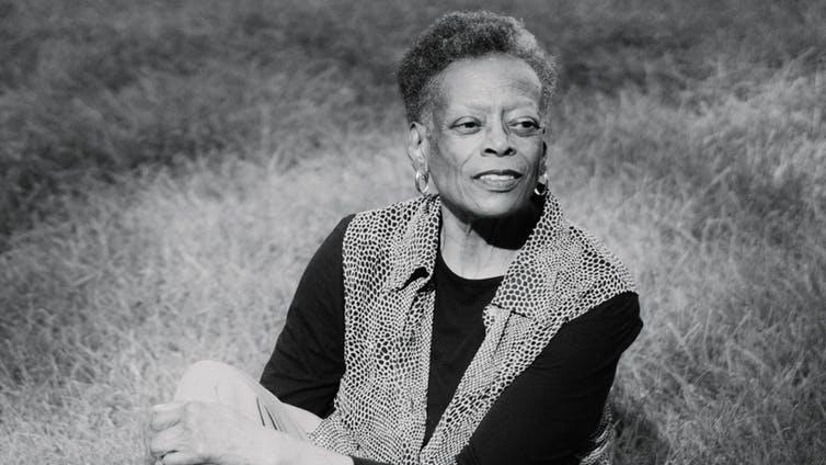 Marcella Wright, one of about 140,000 African American women aging with HIV, sits on the side of a grassy hill smiling. Photo for an article on aging African-American women with HIV.