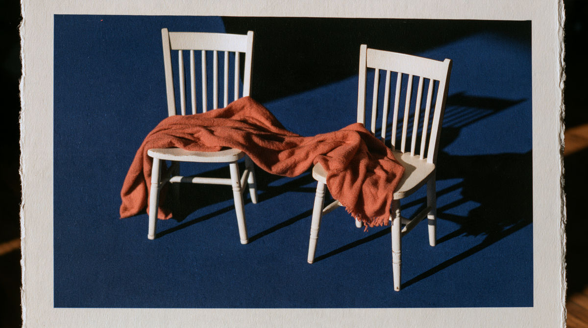 Two white chairs angled apart, connected by a rust-coloured blanket against a navy background.