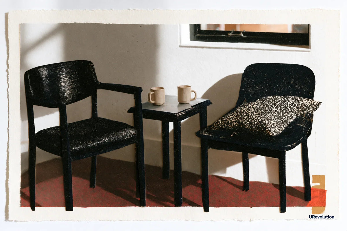Two chairs beside a small table holding two mugs, with a cushion on the right-hand chair.