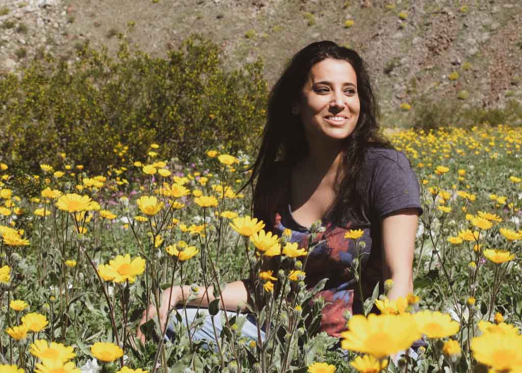 Colourful vintage style photo of Noora Elkoussy siting in a field full of yellow flowers.