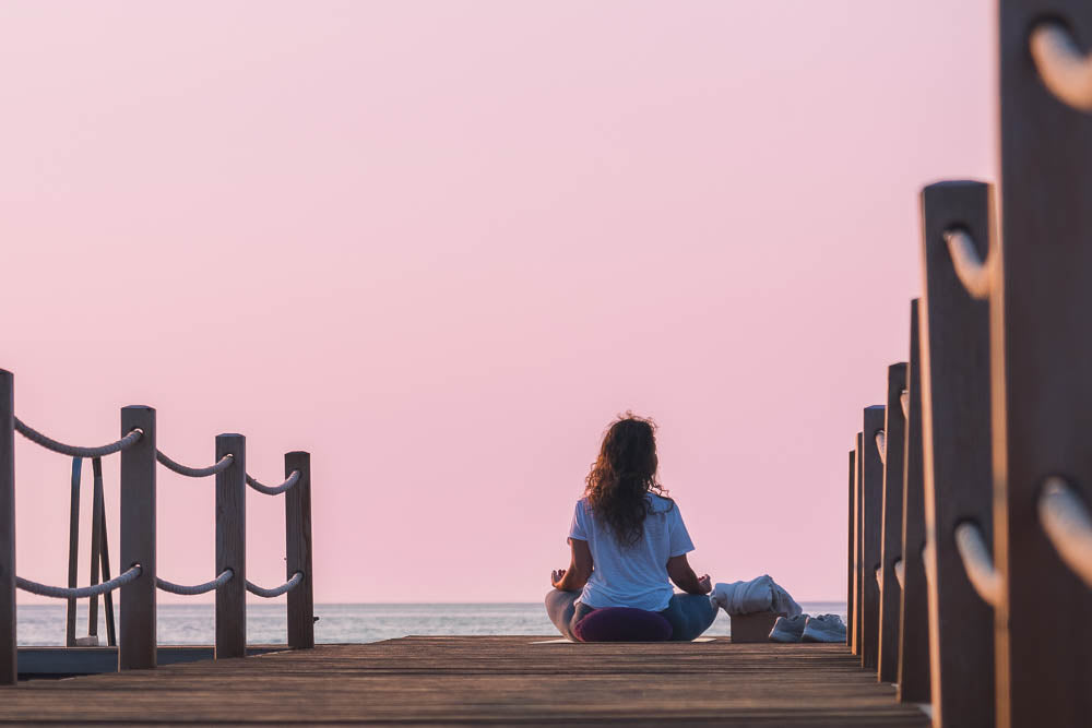 Coping with kidney disease: a person sits at the end of a jetty at sunset in a yoga pose