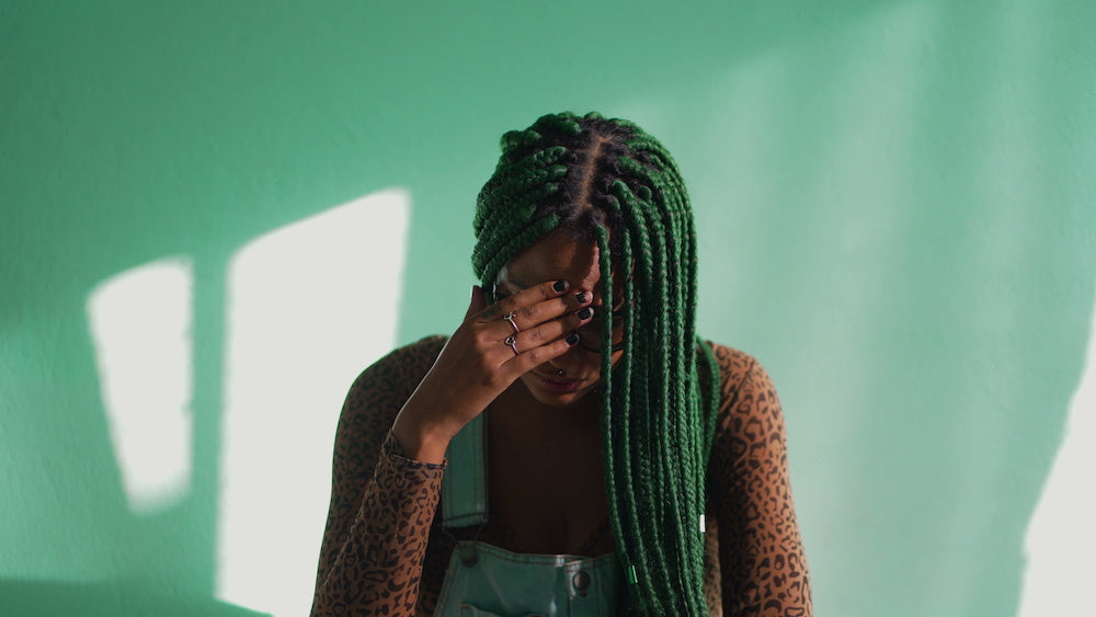 Cystic fibrosis stories: a green-tinted photo of a young Black woman looking down in reflection, pondering a problem. 