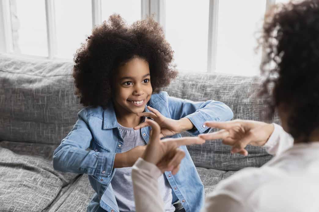 A child and an adult use hand gestures while seated facing one another on a sofa.