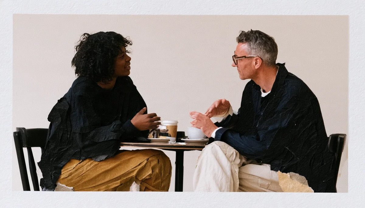 Paper-collage illustration of two adults talking across a café table.
