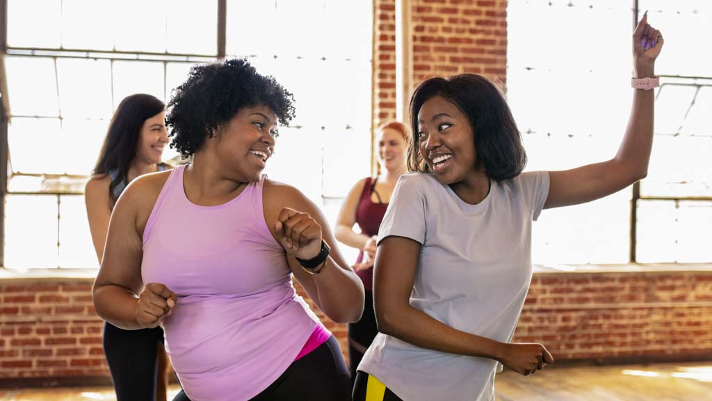 Zumba for disabled people: even though zumba is harder than it looks two African-American women are having in a Zumba class. They bounce their hips together and smile at each other.