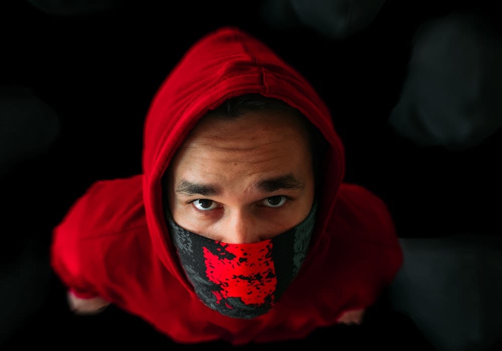 Photo for article on living with coronavirus in a country that disables us. Photo of person in a red hoodie and red and black face mask look up at camera.