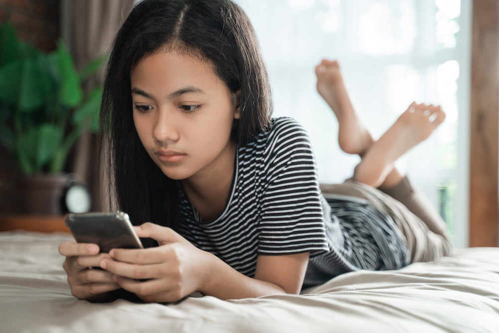 A teenage daughter with type 1 diabetes using a mobile smart phone at home while lying on their bed.