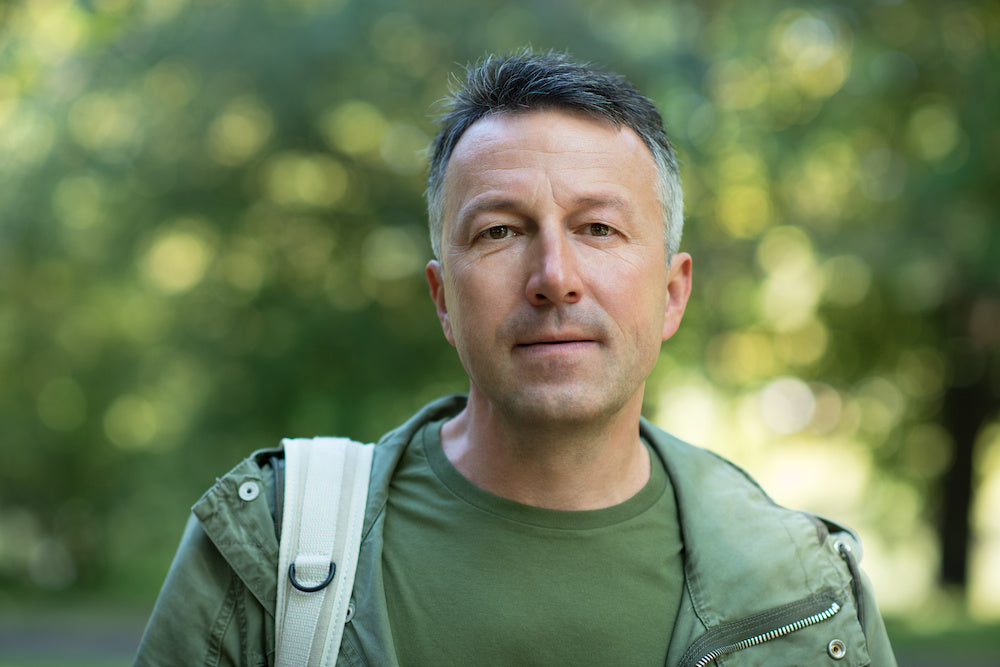 Depression feels like a weight on my chest: a photo of a middle aged man wearing a green jacket in a park. He is looking directly at the camera.