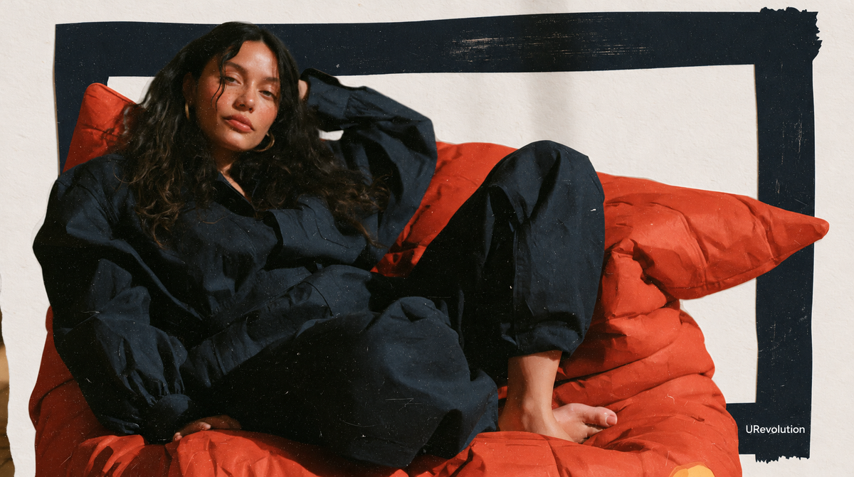 Fictional woman in a navy jumpsuit reclining on a red sofa within a dark painted frame.
