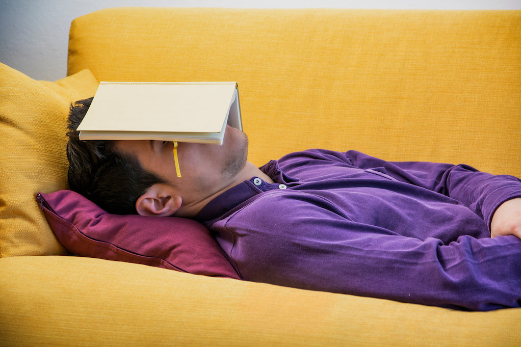 Does terminal cancer make you tired: a man is lying down on a yellow sofa with a book covering their face.