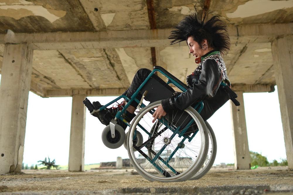 Young man with spiky hair tilts back in his wheelchair in an abandoned building.