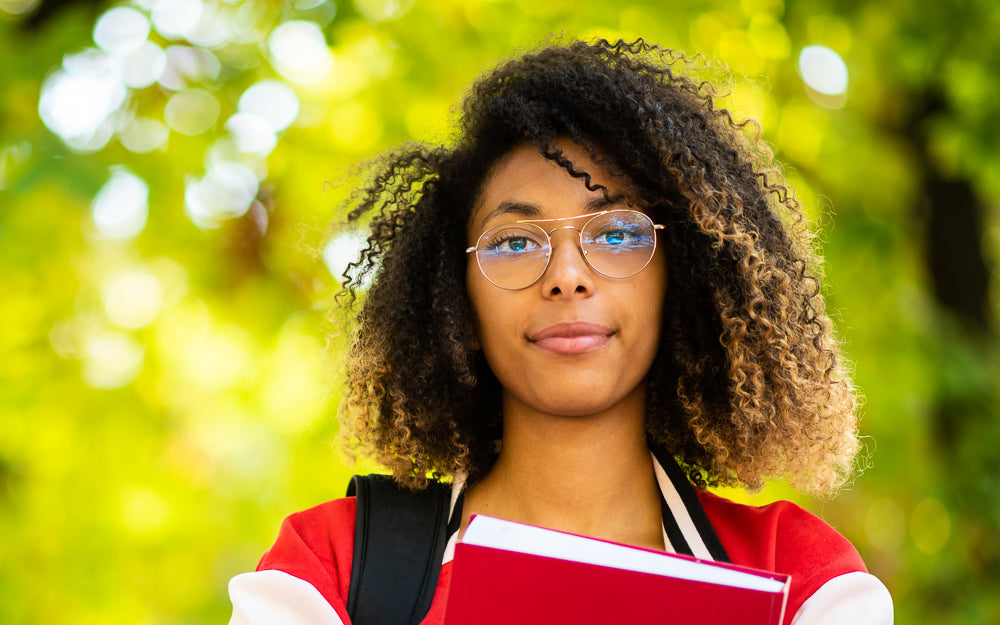 EEC syndrome: a young Black woman is standing outside under some trees. She is wearing glasses and is looking directly at the camera.