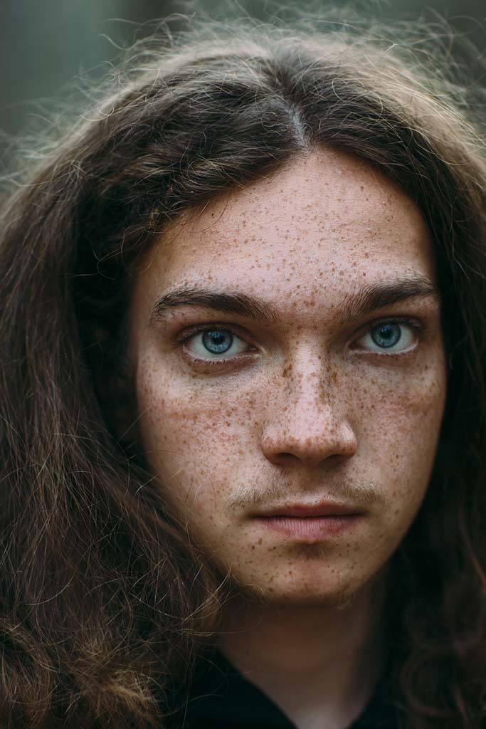 A portrait photo of a man with long red hair, blue eyes, and a freckled face staring at the camera. Image for an article: 