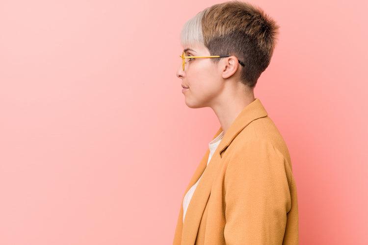 Image for article on: how to interview an Autistic person for a job. Person in casual business clothes gazing left in a sideways pose against a pink background.