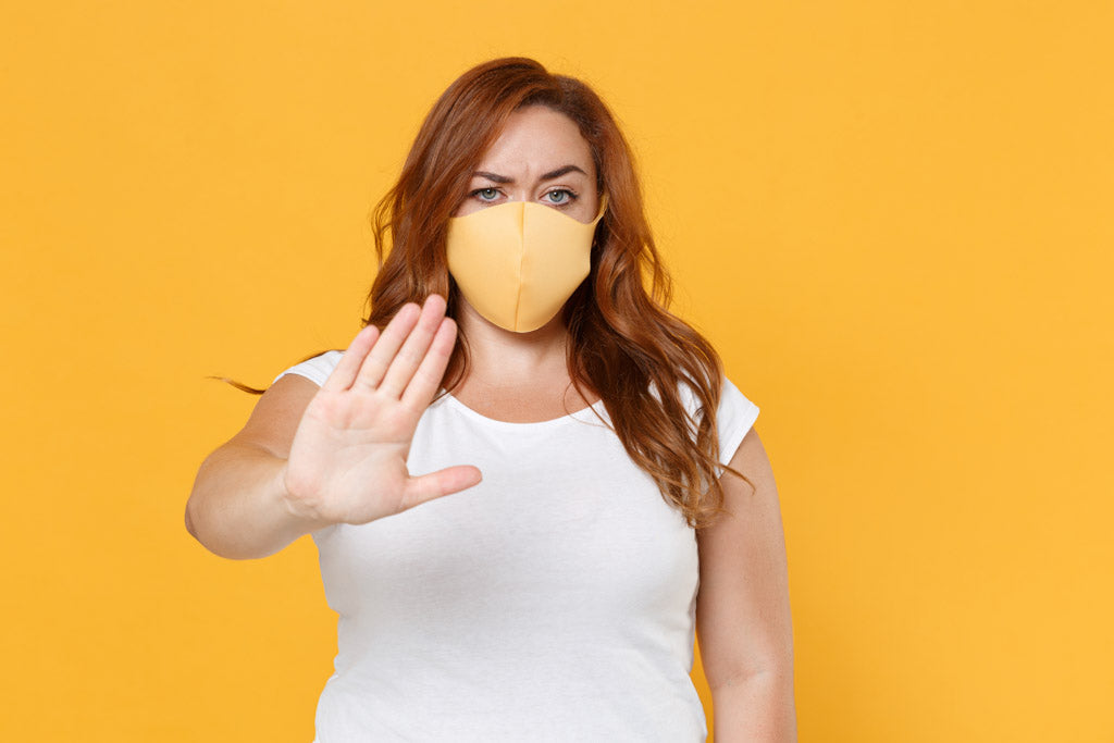 fat shaming doesn't work: a displeased young plus size body positive female is wearing a yellow dress and has a face mask on. She is showing a stop gesture with the palm of her hand towards the camera as if to say, 'stop .. fat shaming doesn't work.'