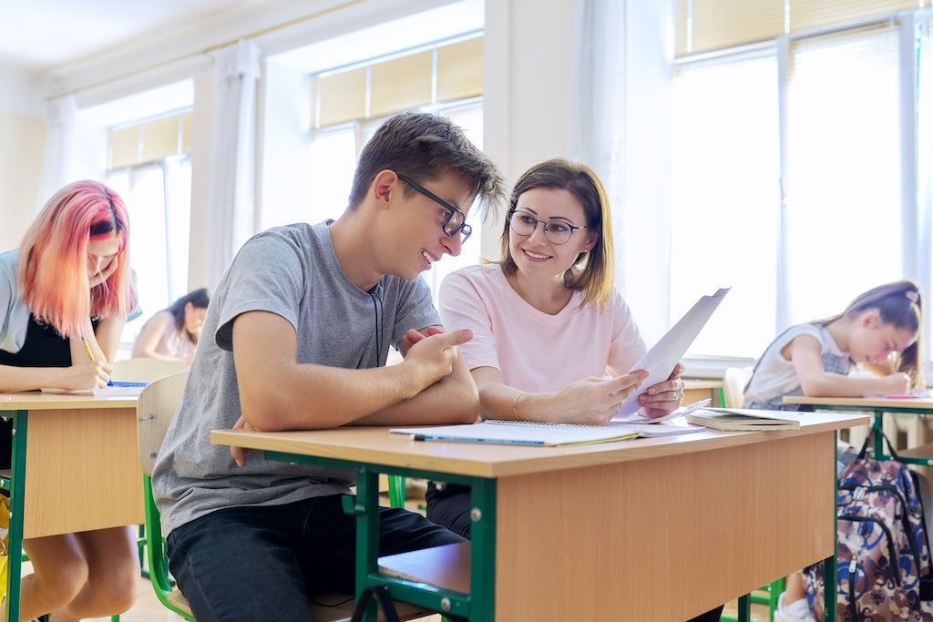 Going to school with a seizure disorder: a teenage boy is sitting at a desk receiving feedback from their female teacher. 