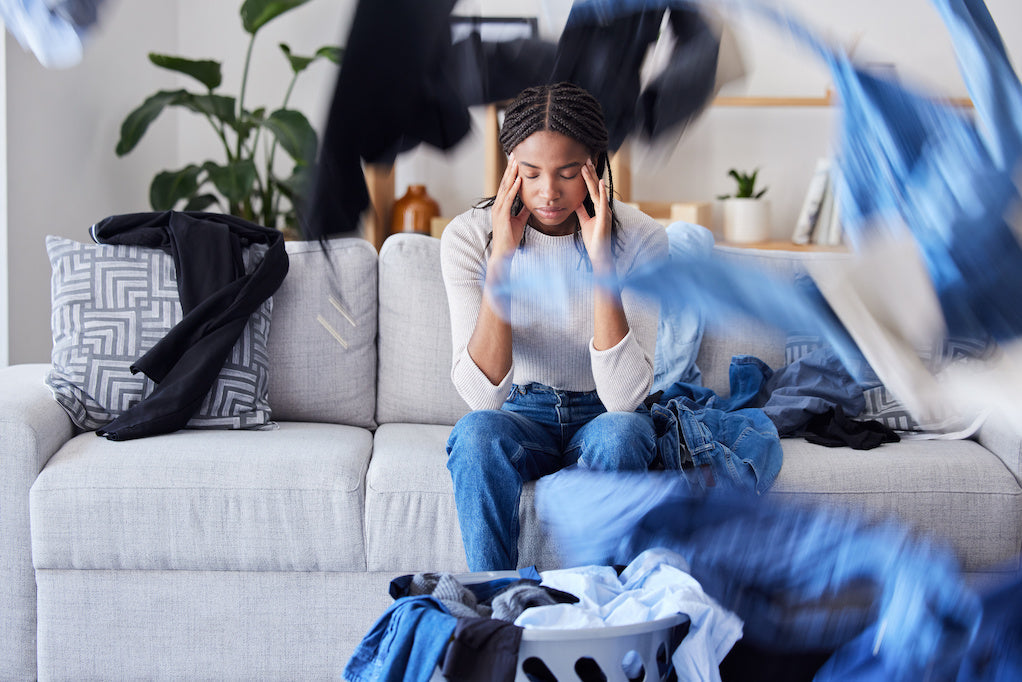 Person sitting on a sofa with their head in their hands as household chores pile up, illustrating fatigue and housework with fibromyalgia.