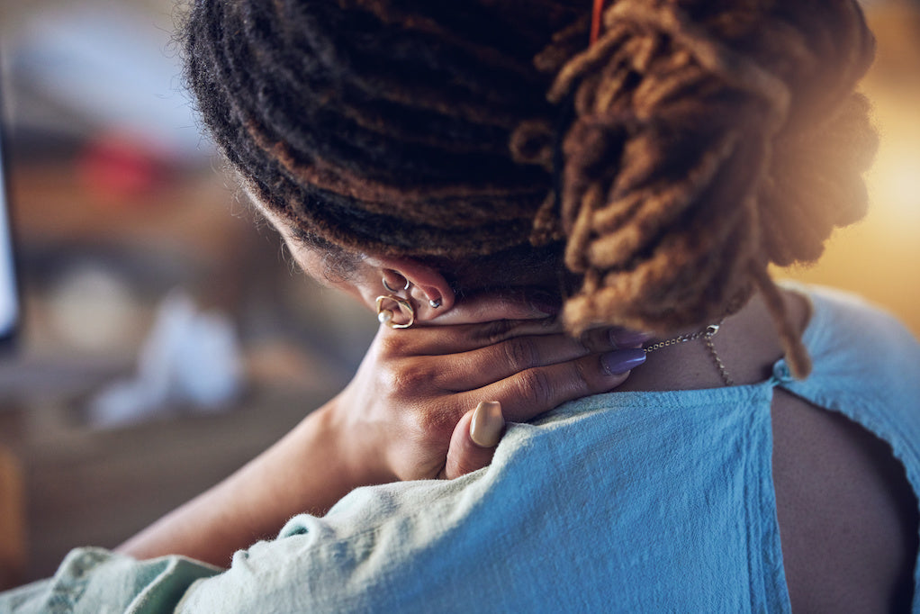 A person with locs resting a hand against the back of their neck.