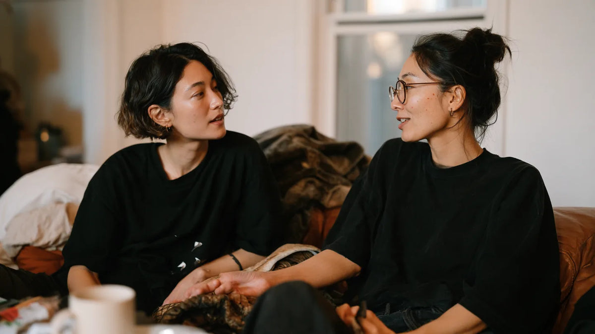 Two friends sitting together on a sofa, talking in a softly lit living room.