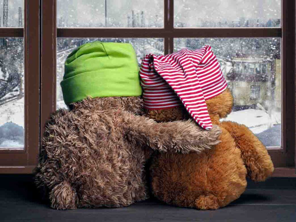 How to help parents after miscarriage? Two friends looking out the window at the falling snow and the city. Toys colorful hats bear cubs. Embrace the window. Concept - love, friendship, support