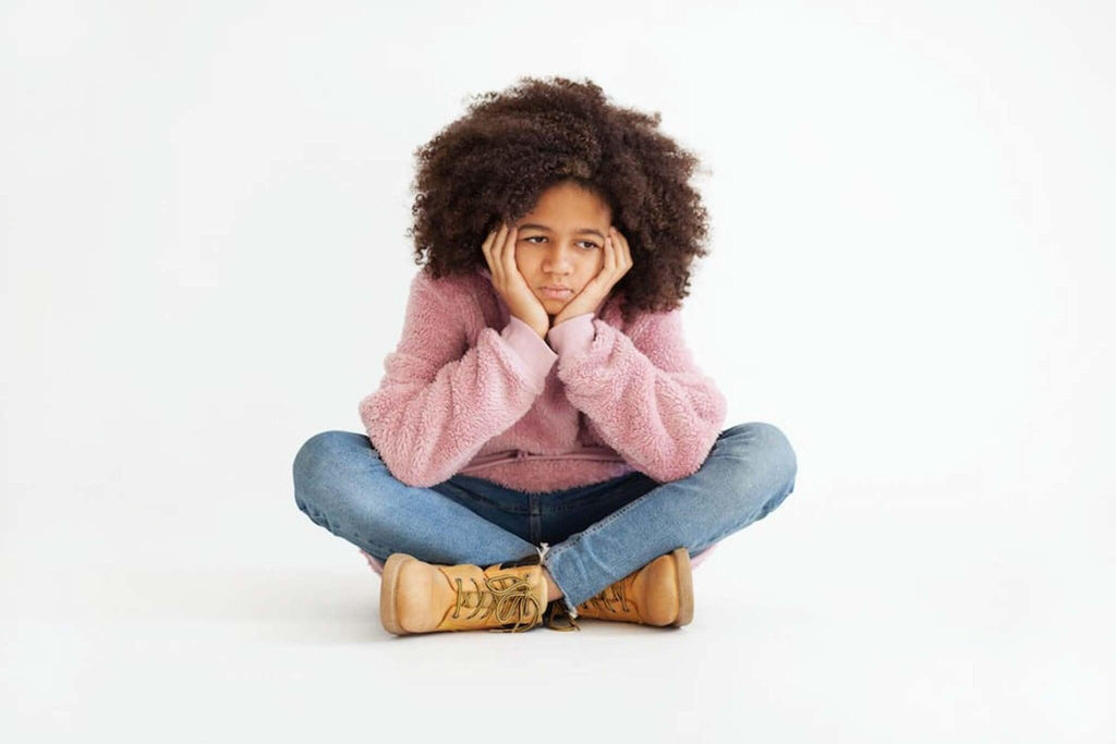 Undiagnosed autism in children: image of young person with big afro sitting forlornly with their legs crossed and chin propped up in their hands.