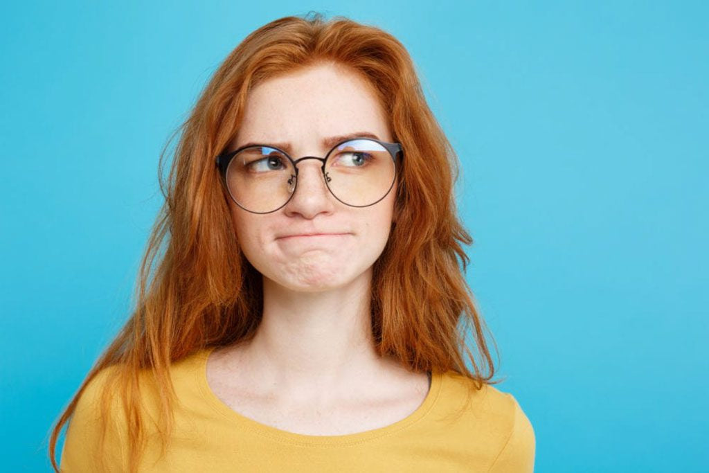 Red-haired woman wearing round glasses against a blue background.