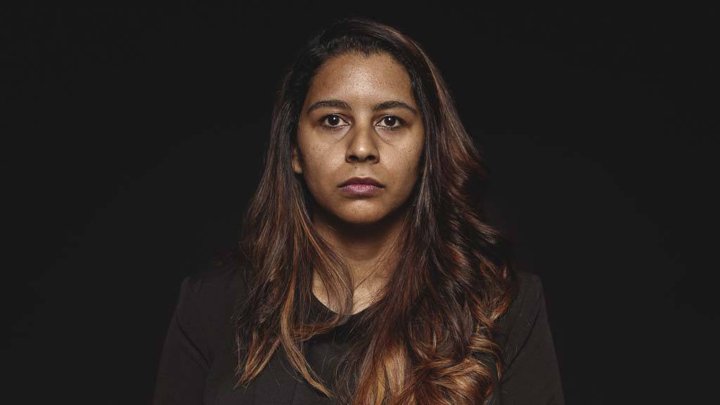 Close up image of a person, against a black background, with a serious expression on their face staring at the camera. Image for an article on how to tell someone they have cancer.