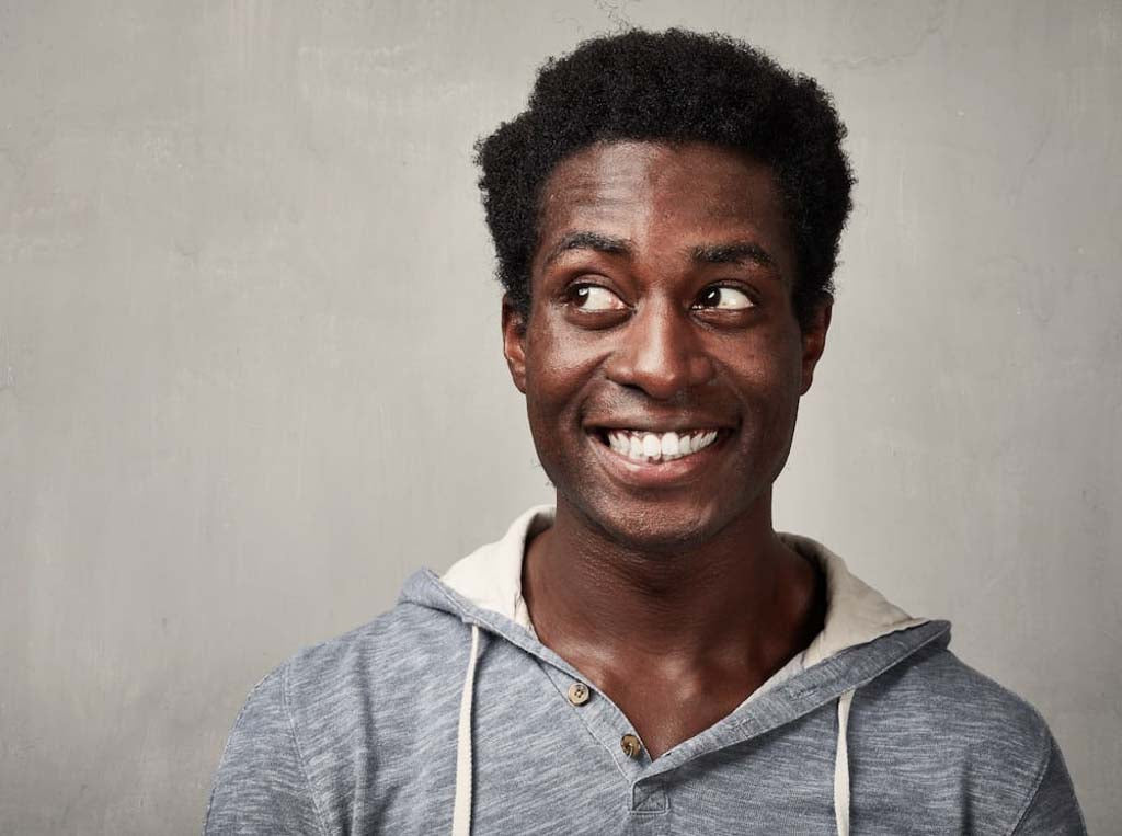 Man in a gray hoodie smiling broadly and looking to one side.