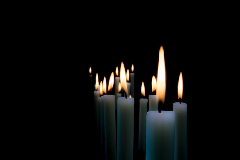 Rows of lit white candles against a dark background.