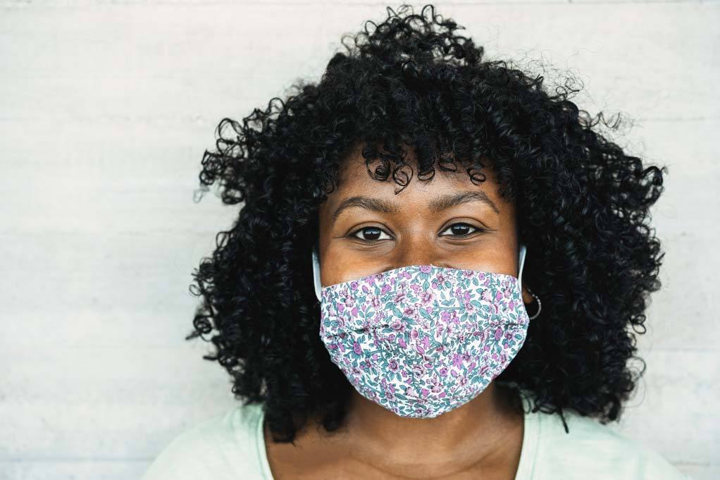 Obsession with cleanliness and hygiene: photo of a happy young black woman smiling under a protective face mask during the coronavirus pandemic.