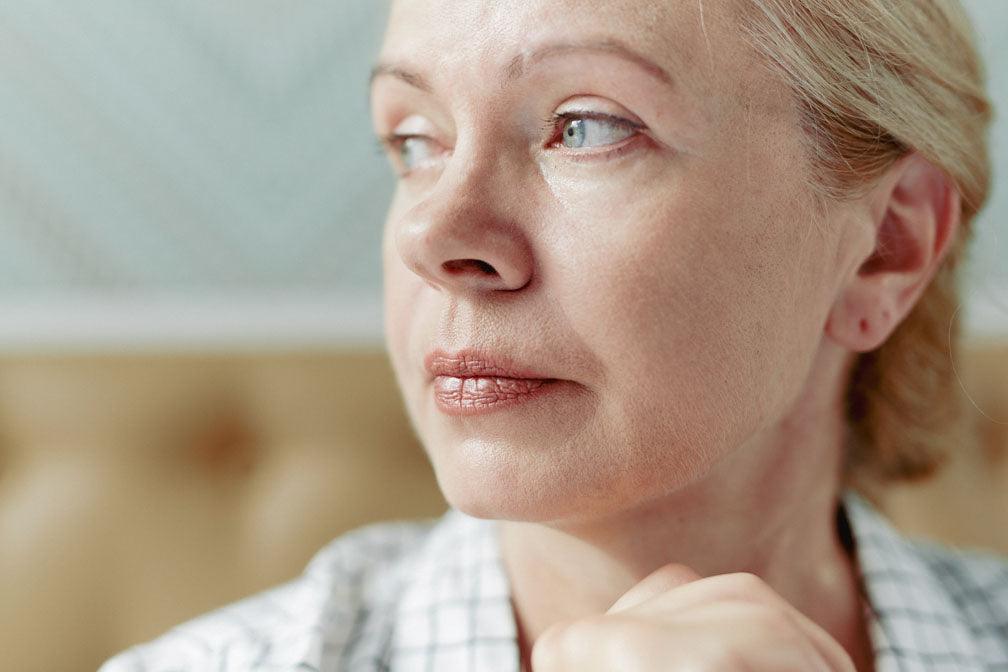 Endometriosis, anxiety, and depression: headshot of a middle-aged woman with deep gray-blue eyes looking away pensively against a blurred background.