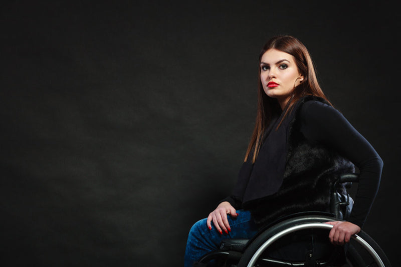 Growing up with cerebral palsy: young woman in wheelchair looks at camera from left side of photo. She is wearing a black vest and blue jeans with black boots. 