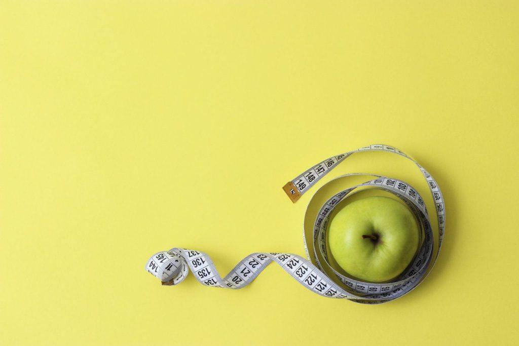 Learning how to hide anorexia from parents and friends nearly destroyed me: image of an apple wrapped in tape measure against a yellow background.