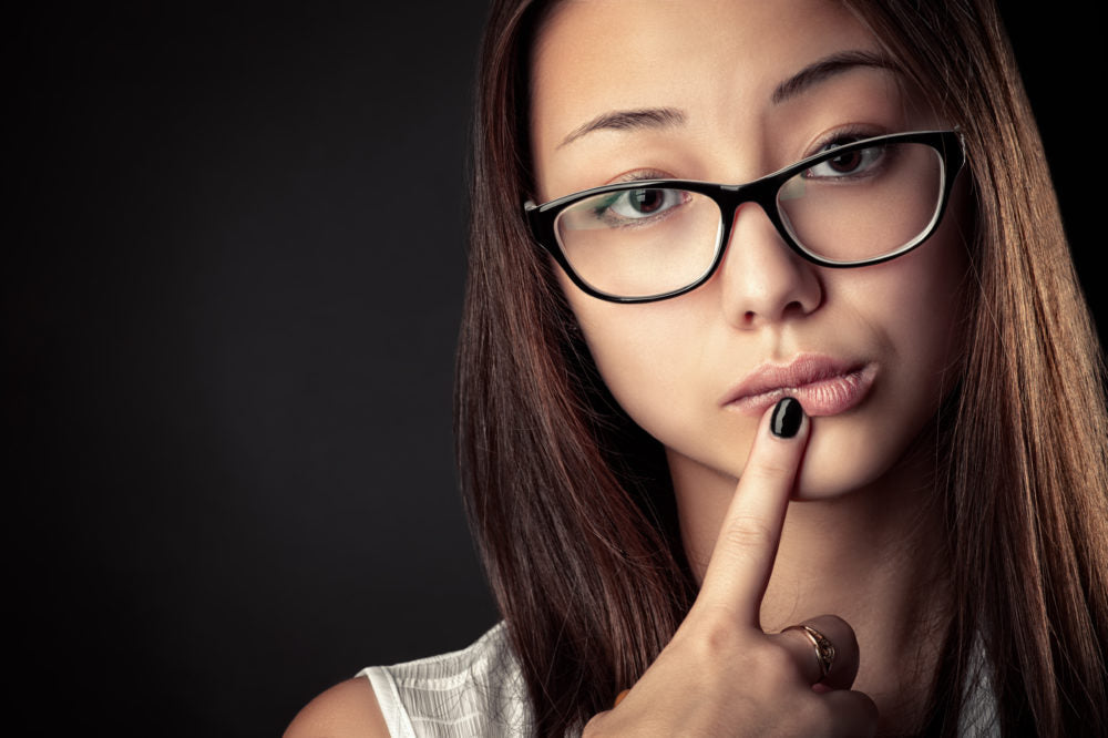 Stock portrait of a person wearing glasses, with a finger resting against their lips.